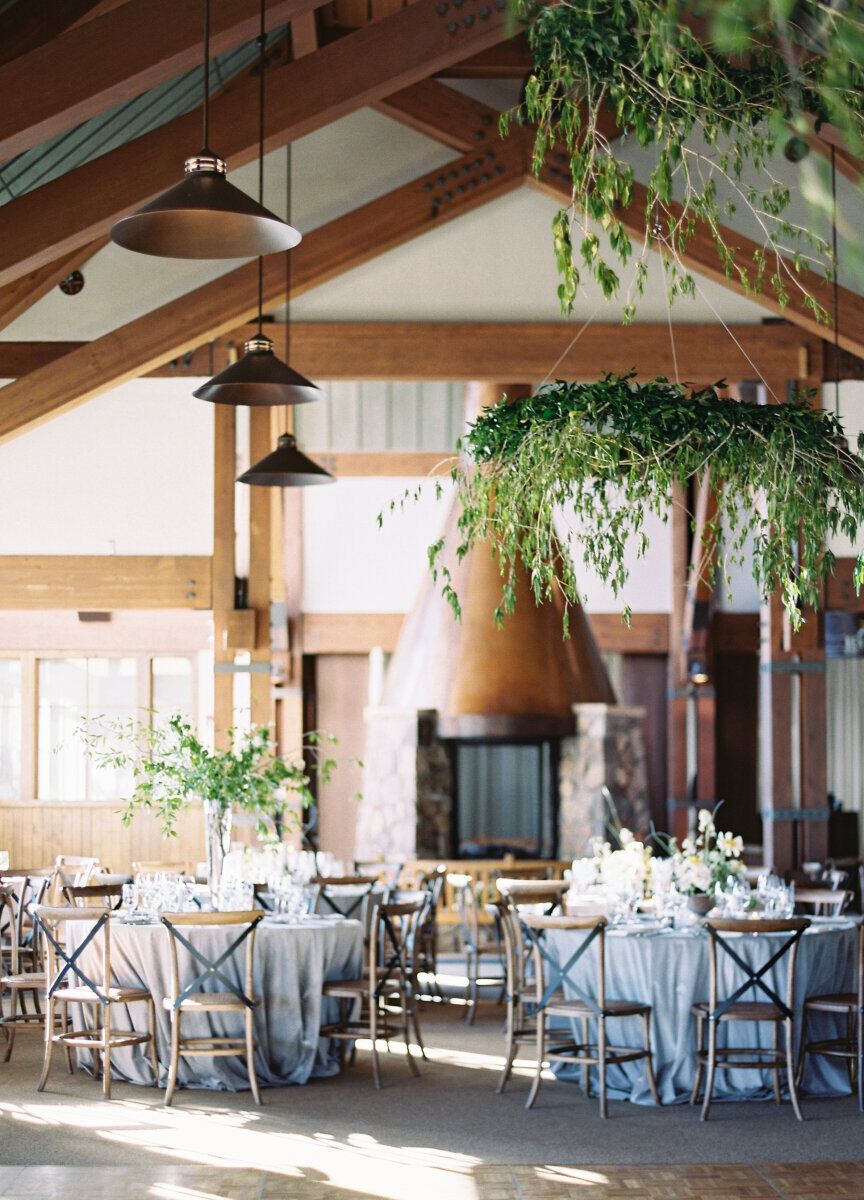 Wedding budget: Understated light blue wedding reception in event space with vaulted ceilings and exposed beams featuring hanging greenery installation 