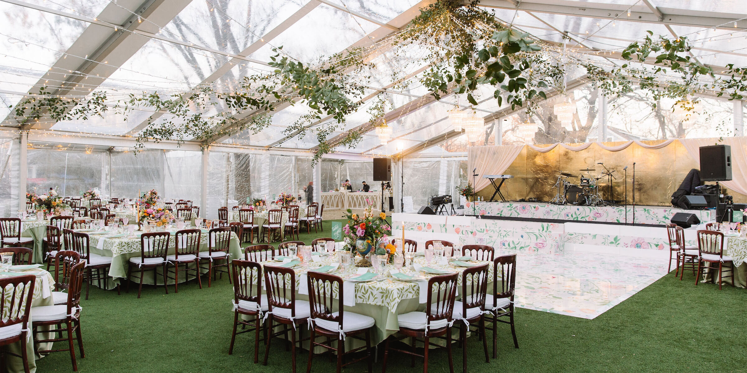 Floral themed wedding reception set up under clear top tent with hanging greenery.