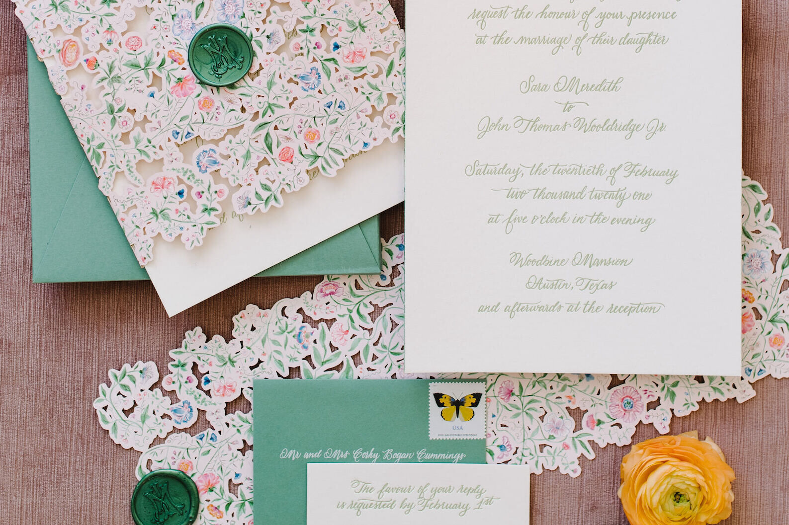 A wedding invitation suite with calligraphy and floral illustrations, and its soft green envelope ready to be sent using assorted vintage postage stamps.