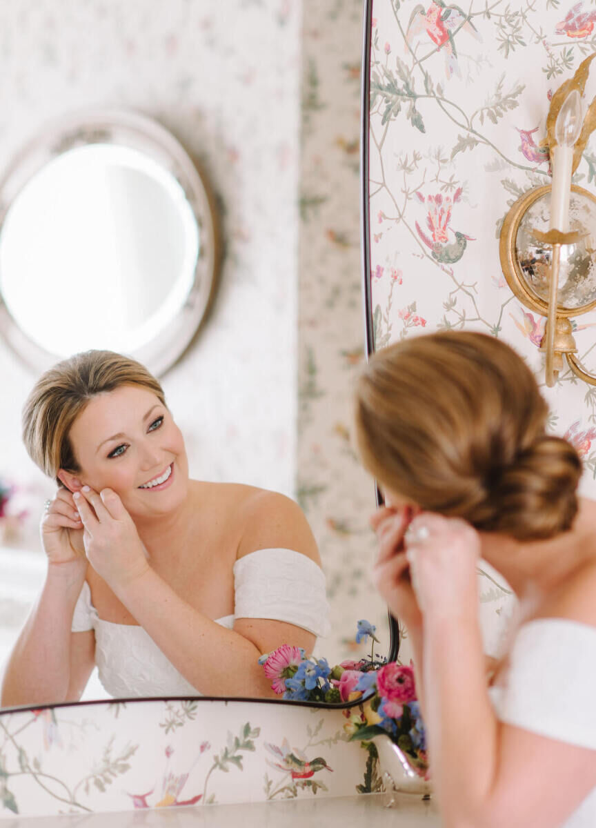 A bride puts her earring in at the mirror in the room where she gets ready for her Texas wedding.