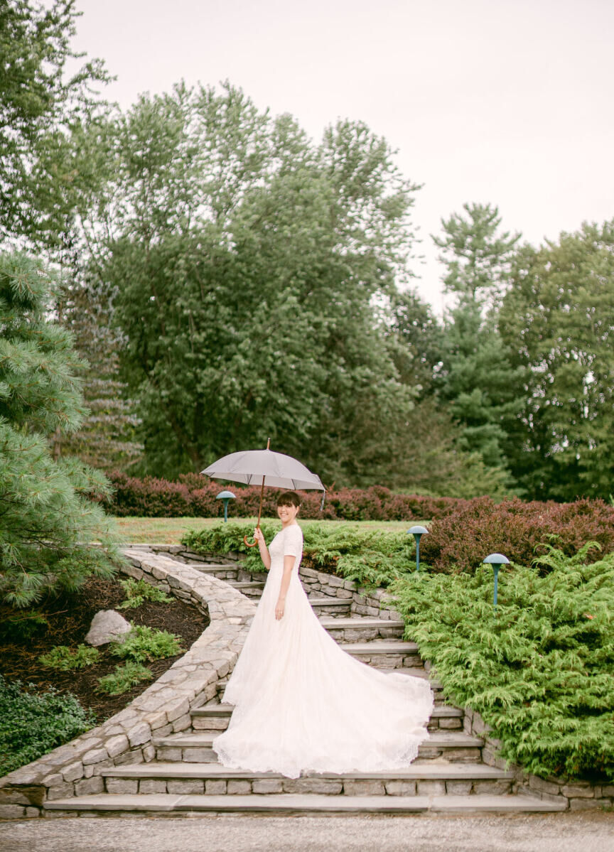 Wedding details: A bride holds and umbrella and smiles during a rain shower before her wedding ceremony.