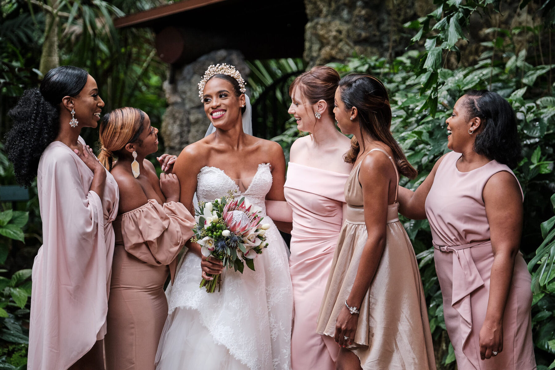 Wedding Dress Shopping: A bride smiling surrounded by her bridal party, all of whom are dressed in pink.