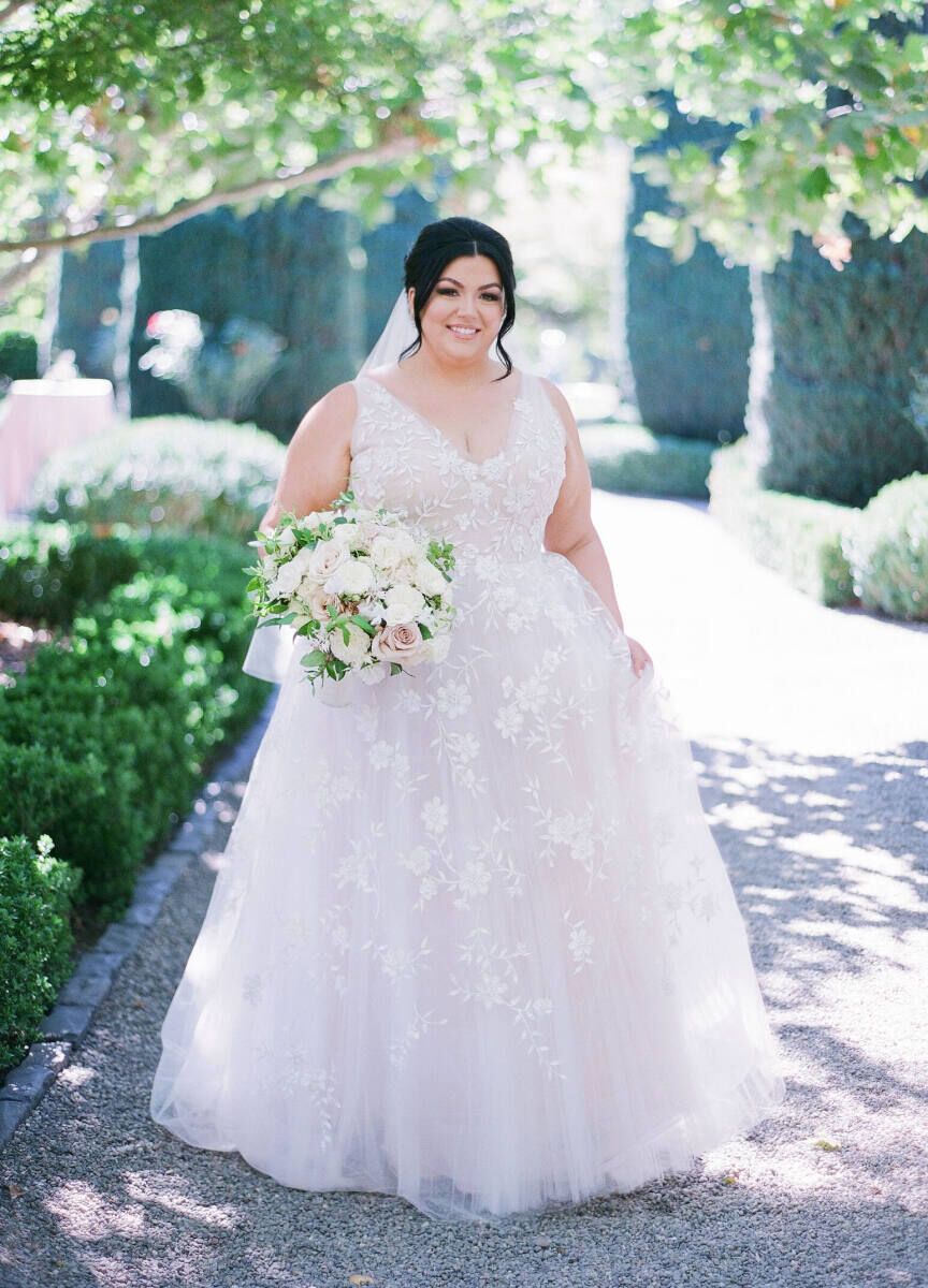 Wedding Dress Shopping: A bride in a ballgown with floral applique holding an all-white bouquet.