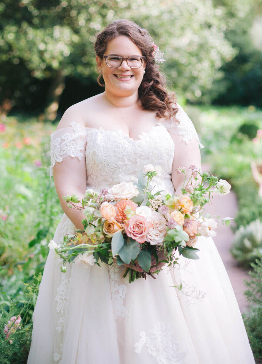 Wedding Dress Shopping: A bride wearing glasses and an off-the-shoulder lace gown, holding a multi-colored floral bouquet.