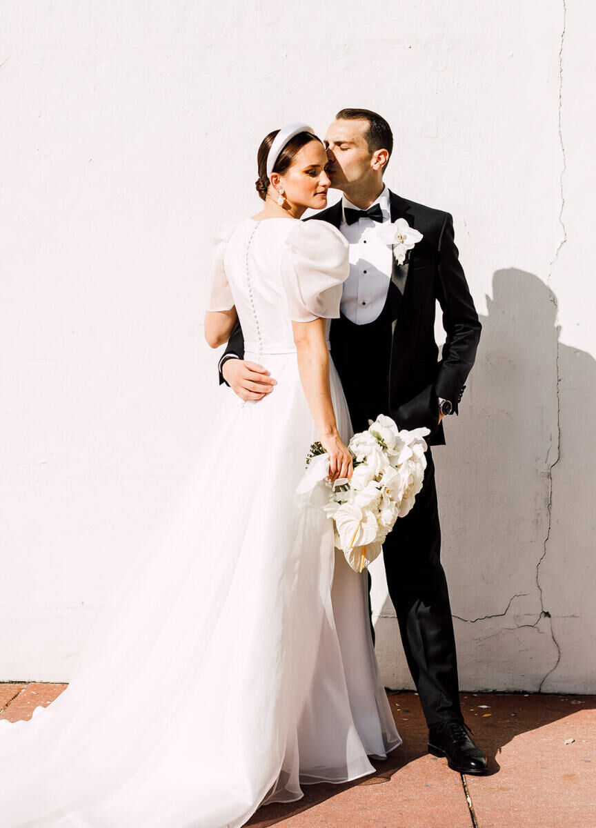 Wedding Dress Shopping: Classically dressed bride and groom posing in front of a blank concrete wall.