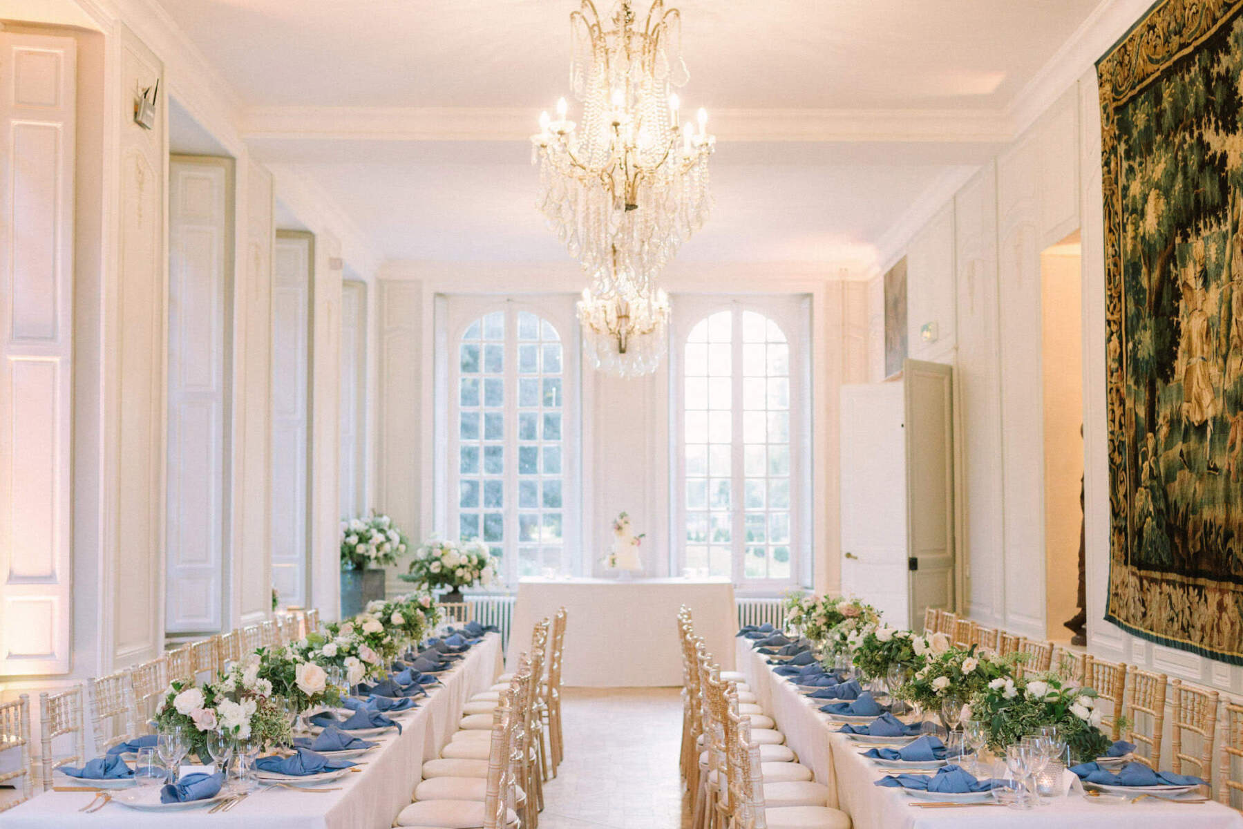Wedding Etiquette Budget: An indoor reception setup with chandeliers hanging above and blue tablescapes.