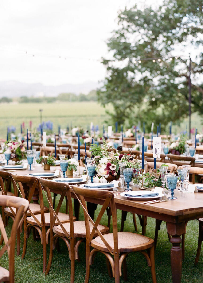 Wedding Etiquette: An outdoor reception setup with wooden tables and chairs and blue candles, cups and napkins on the table.