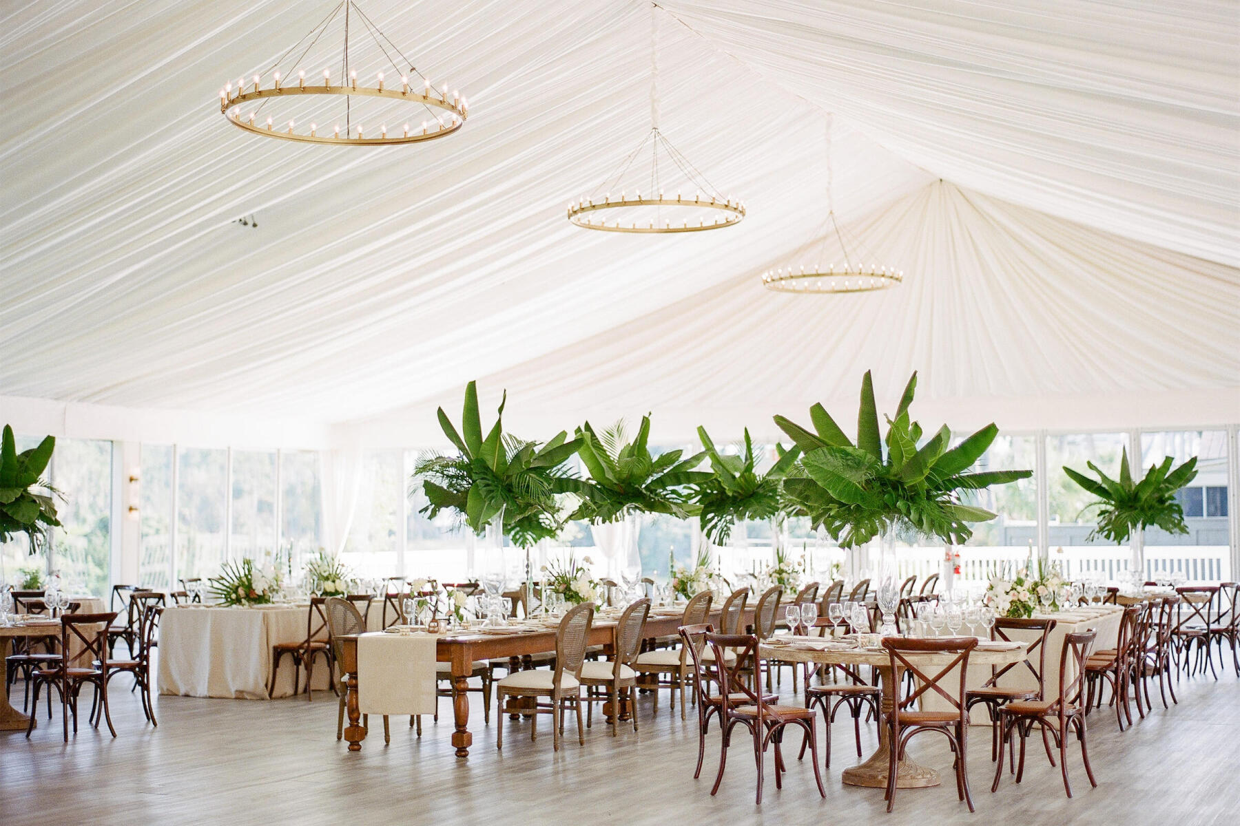 Wedding Etiquette Budget: Cream colored draped wedding reception tent with neutral tables and chairs, and centerpieces of large palm fronds.