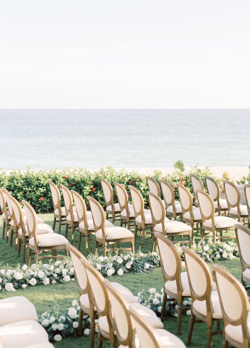 A ceremony setup overlooking the ocean in Mexico, with white and wood chairs and a white flower-lined aisle.