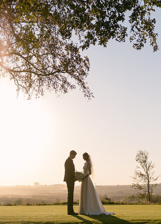 Wedding News: A bride and groom posing at the Omni PGA Frisco Resort under a tree at dusk.