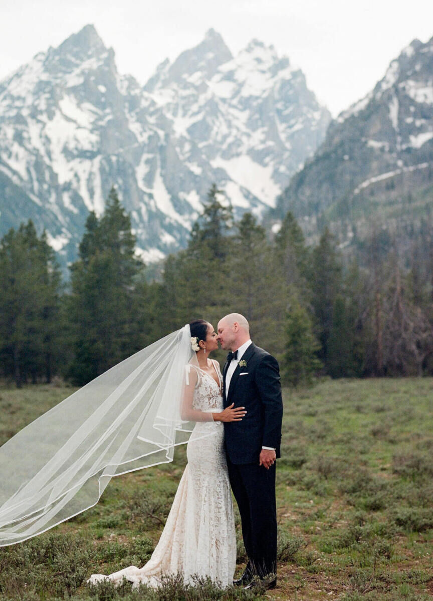 Wedding Photography Ideas: A bride and groom almost kissing in a grassy area with forest trees and mountains in the background.