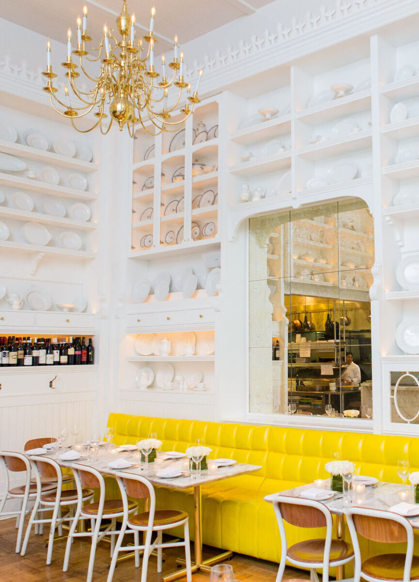 Wedding Photography Ideas: An all-white room in a restaurant with open shelves, a gold chandelier and a bright yellow booth seating option.