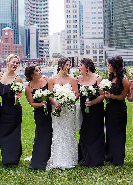 Wedding Photography Ideas: A bride smiling at her bridesmaids, who are wearing black dresses and holding white bouquets, in Chicago.
