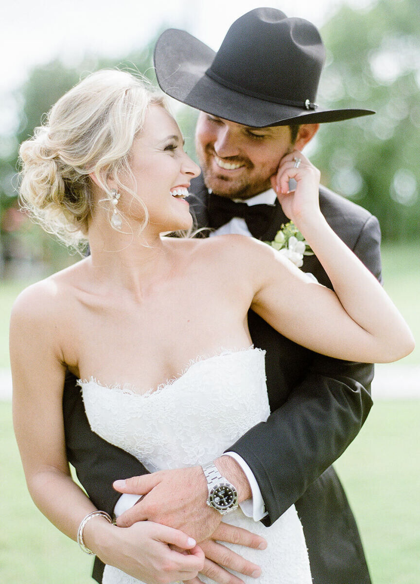 Wedding Photography Ideas: A groom in a cowboy hat, wrapping his arms around a bride as they smile at each other.