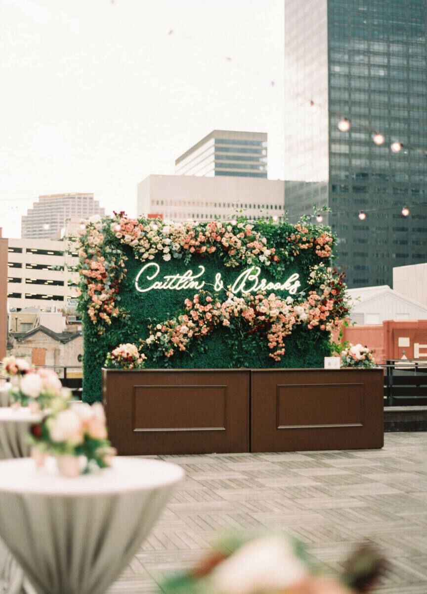 Wedding Photography Ideas: A bar on a rooftop with a greenery wall with flowers and the couple's names on it.