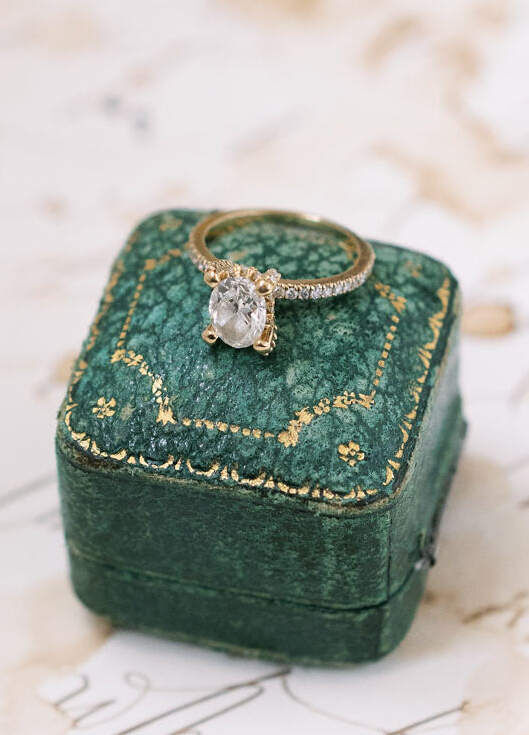 Weddng Ring Design: An oval cut engagement ring with a pavé setting on top of an evergreen square ring box.