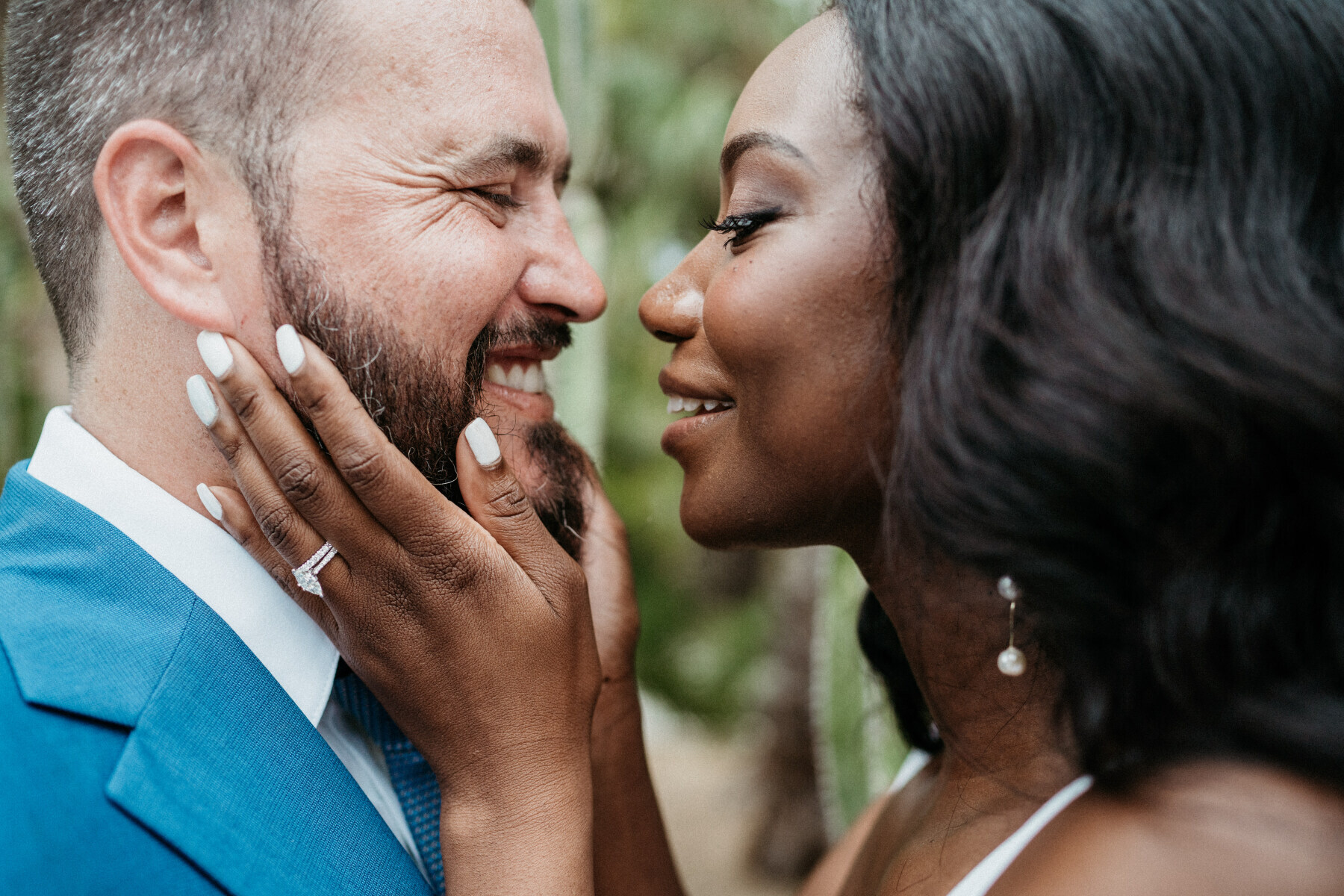 Wedding Ring Design: A bride holding a groom's face in her hands as they lean in to one another. Her marquise diamond ring can be seen on her ring finger.