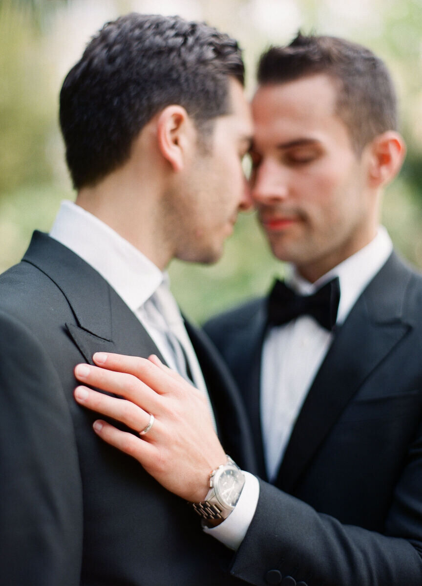 Wedding Ring Design: A groom laying his hand on another groom's chest with his wedding band on his ring finger.