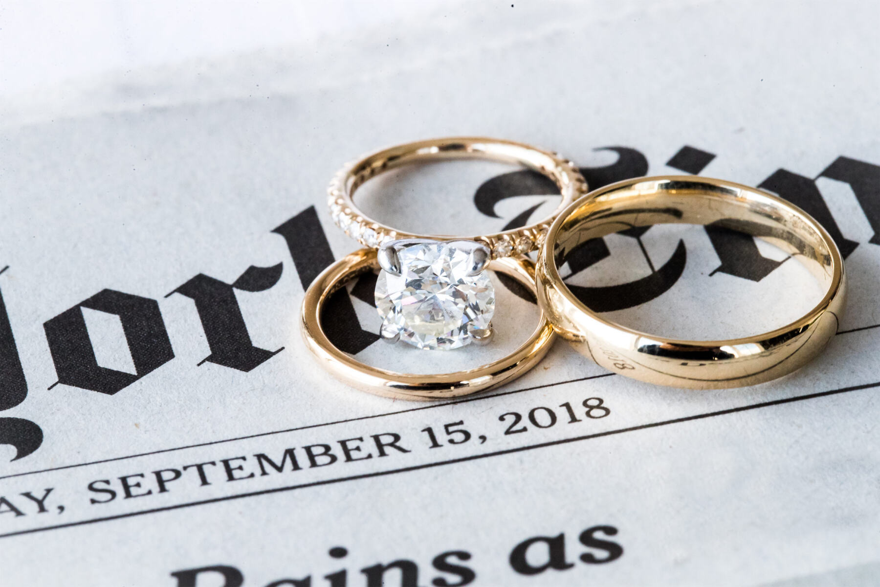 Wedding Ring Design: A round cut diamond engagement ring and two golden wedding bands sitting on top of the front page of the New York Times.