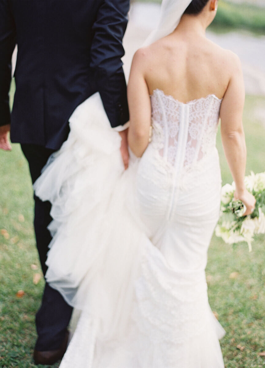 A close-up shot of a bride and groom walking away in a grassy area.