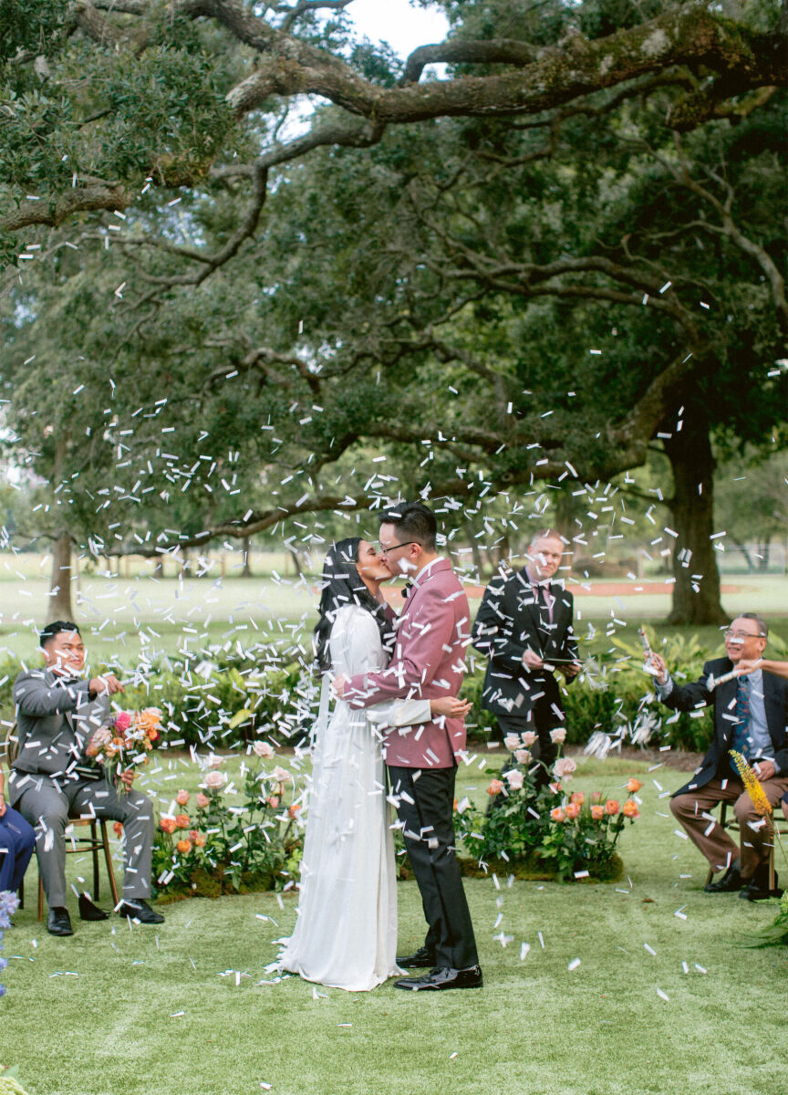 Wedding Tips: A newly married bride and groom kissing outside at their outdoor ceremony while confetti rains down around them and loved ones cheer.