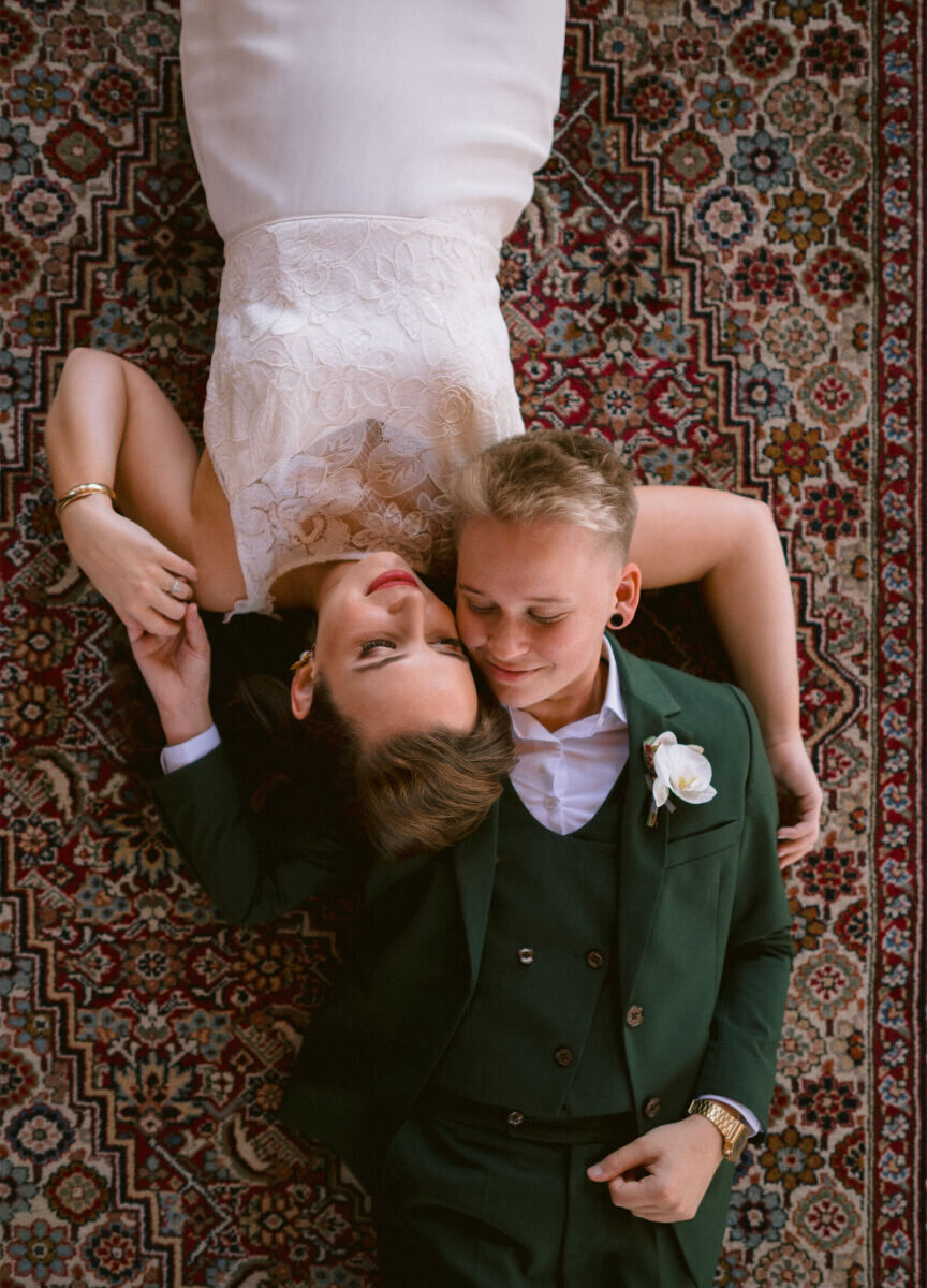 Wedding Tips: Two newlyweds lying on a rug in opposite directions with their heads and hands are embracing.