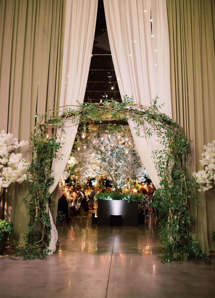 Wedding Tips: An arch made with greenery sitting in front of green and white curtains that lead into a reception space.