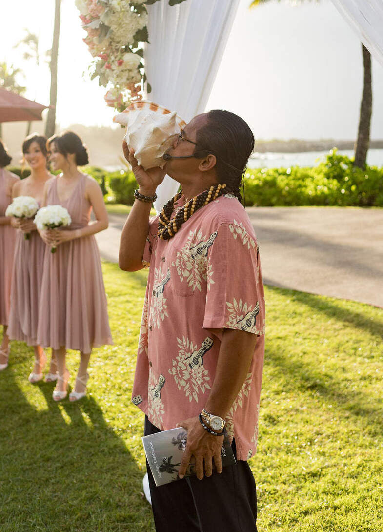 Wedding Tips:  A person blowing into a conch shell at an outdoor wedding ceremony in Maui, Kapalua.