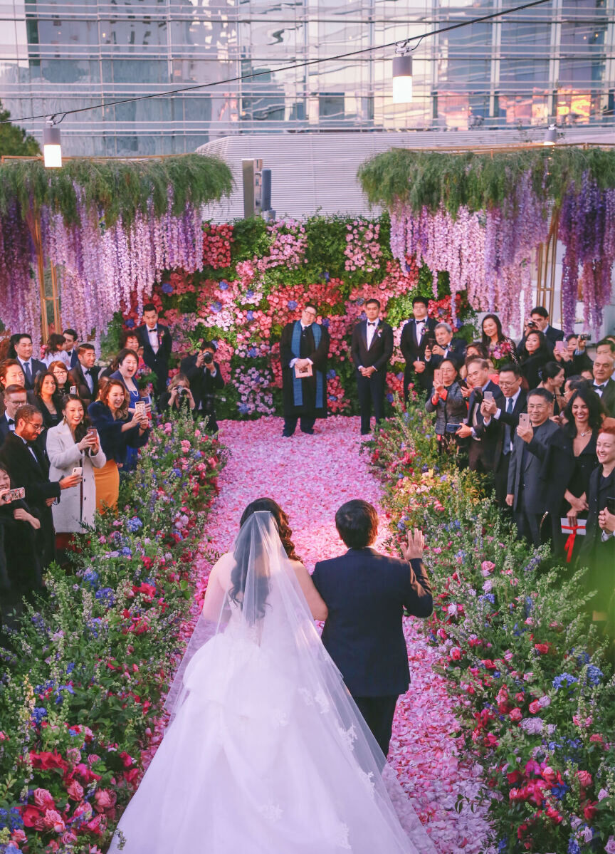 Best Wedding Venues for Creative Couples: A bride being escorted down a floral aisle at Aria.