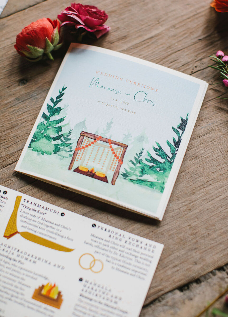 Wedding Website Examples: A flat lay of a wedding invitation and itinerary with red flower on a wooden table.