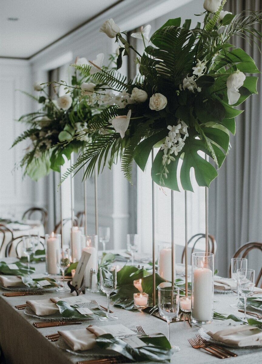 Wedding Website Examples: A reception table with hanging floral arrangements with oversize tropical leaves and white flowers.
