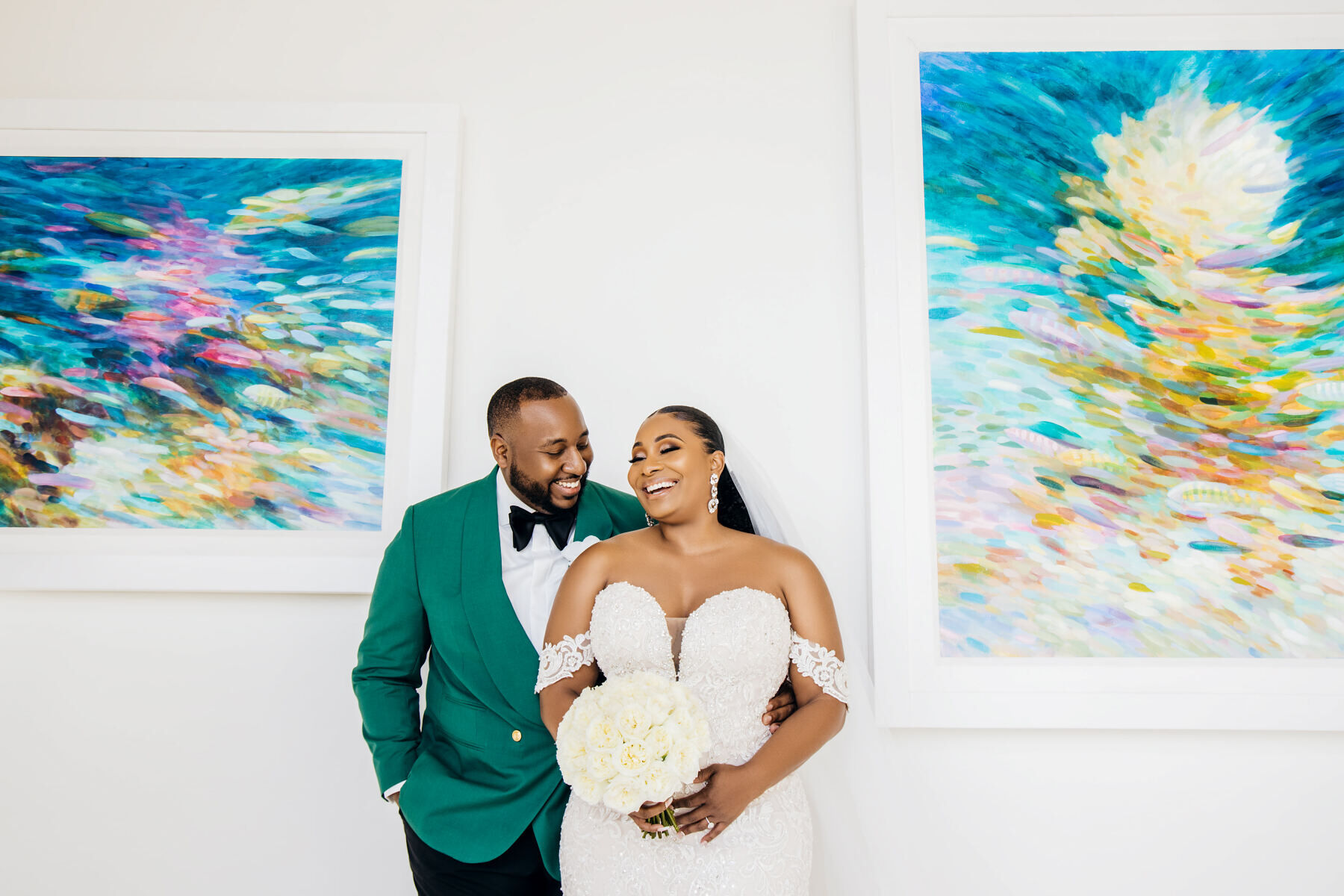 Wedding Website Examples: A bride and groom laughing while posing in front of two art pieces.