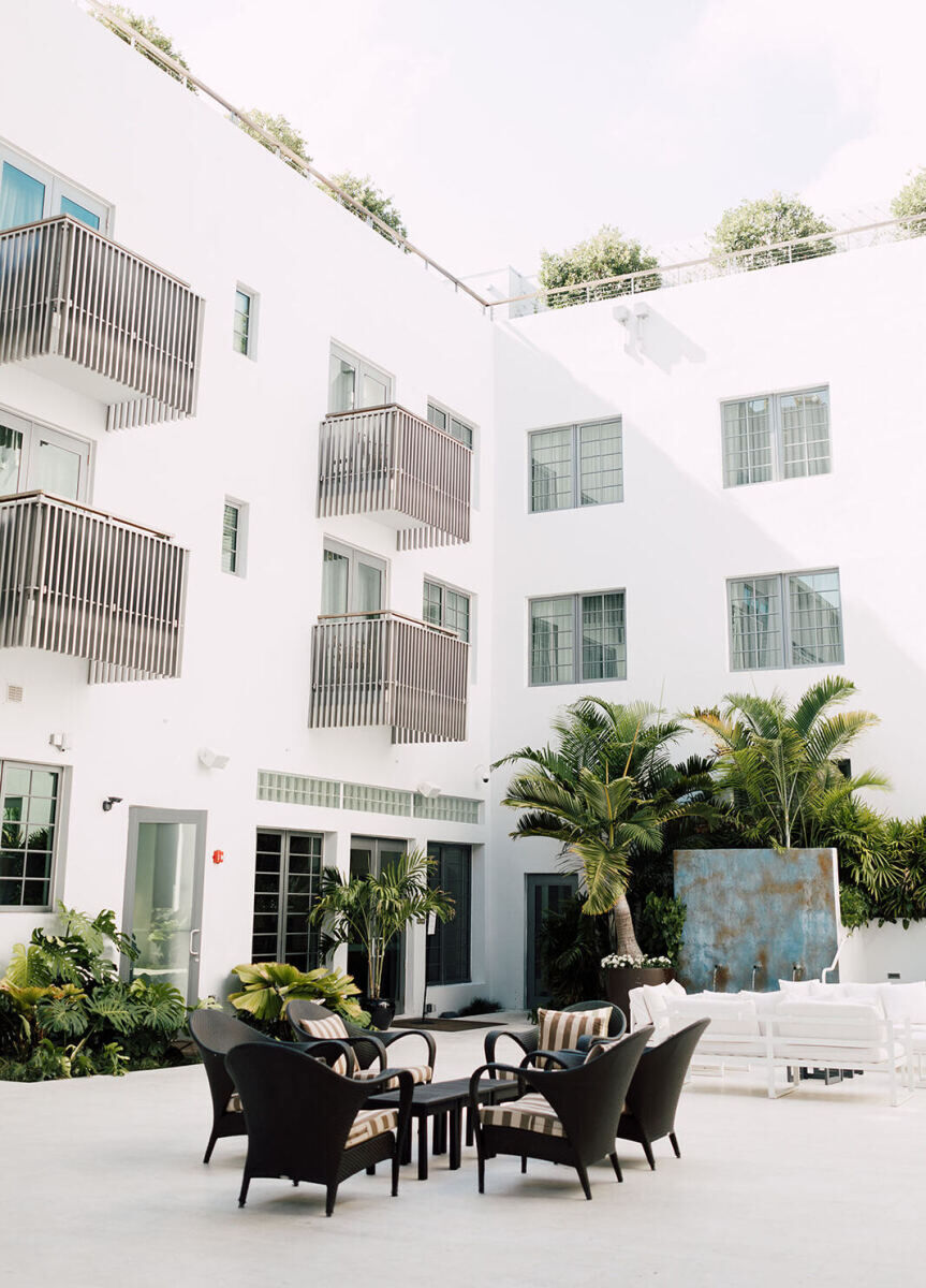 Wedding Website Examples: A courtyard at a white-painted hotel in Miami with chairs and other seating options.