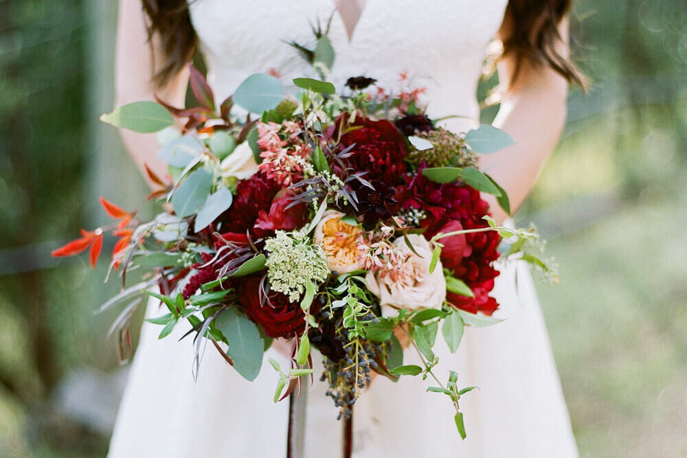 Wedding Website Examples: A bride holding a red, pink and green floral arrangement.