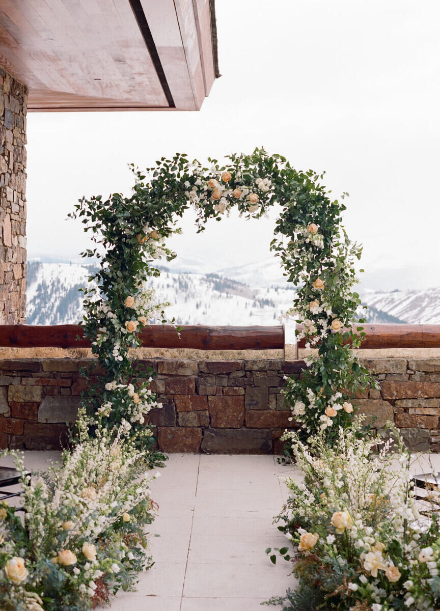 Winter wedding details: Greenery adorned wedding ceremony arch and aisle on resort balcony, overlooking the snow covered mountains.