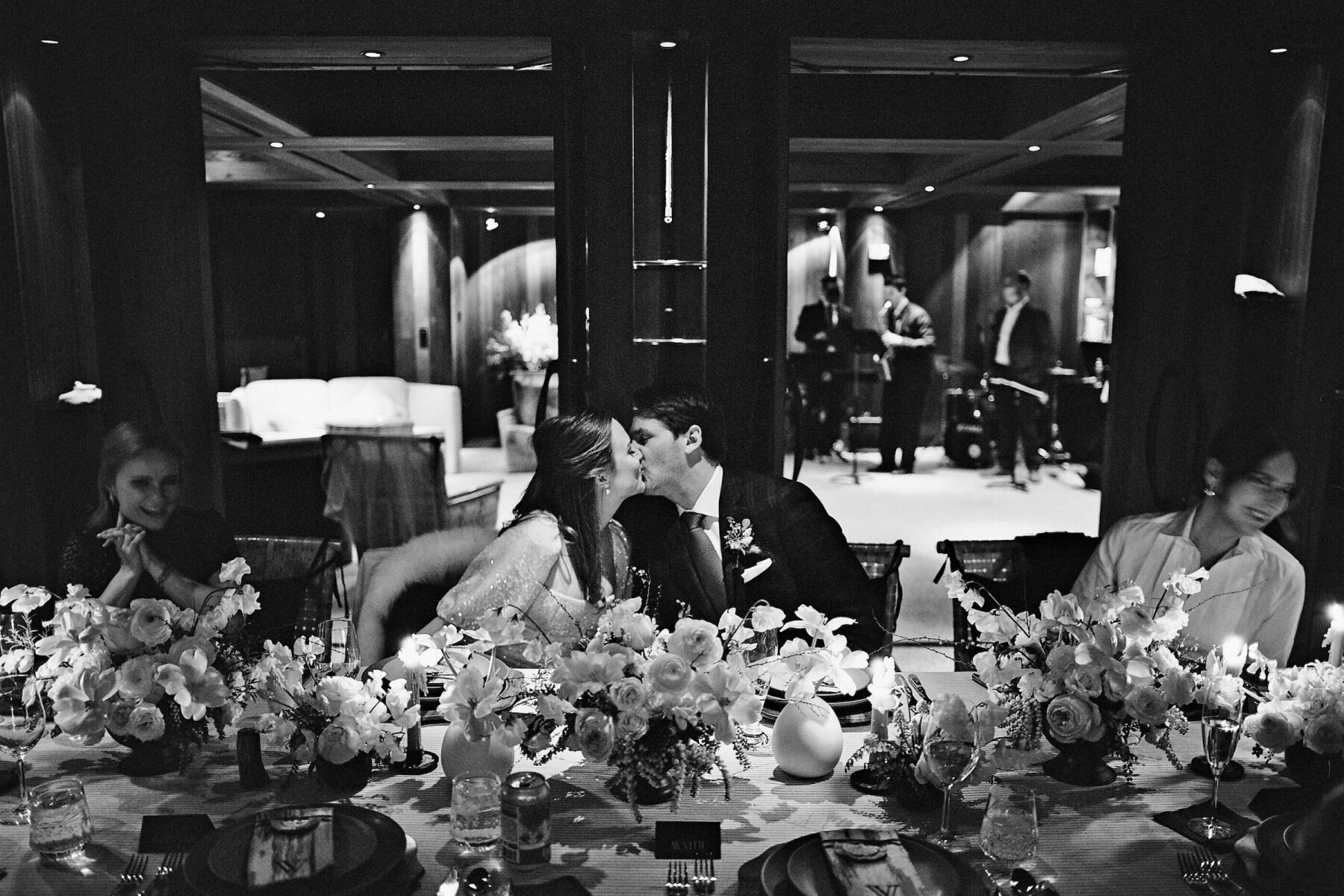 Winter wedding details: A bride and groom share a kiss during their wedding dinner as musicians play in the background.