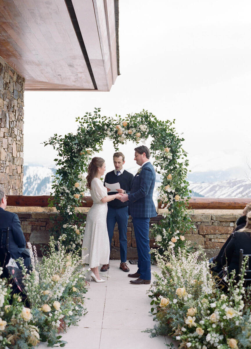 Winter wedding details: An officiant performs an outdoor wedding ceremony in front of a floral arch in Wyoming.