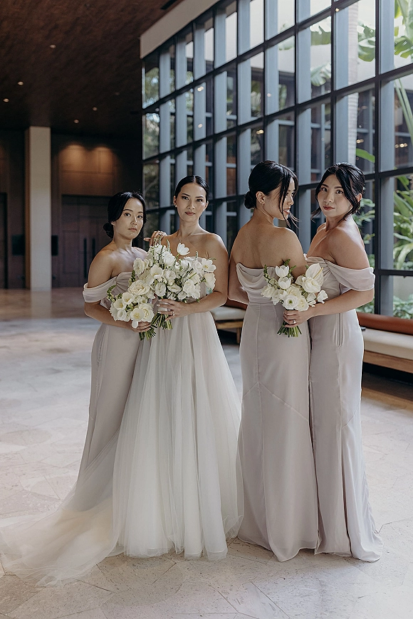 Bridesmaid group portrait of bridesmaids with bouquets beside the bride in a modern window-lit hallway with indoor plants and stone floors