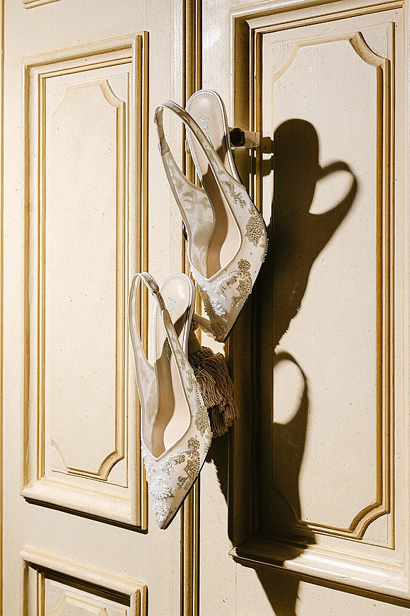 Wedding shoes in ivory bridal heels style, slingback pointed toes with lace applique and beading on paneled doors in warm sunlight