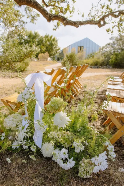 Ceremony aisle flowers elevate outdoor ceremony decor, natural clusters lining the aisle and accented by simple white ribbon bows.
