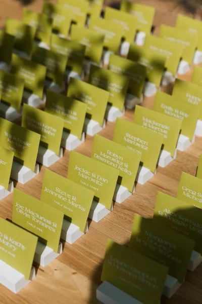 Escort card display arranged on an escort card table, rows in neat card holders atop a sunlit wooden table with soft, dappled shadows.