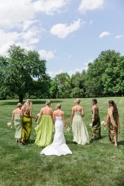 Bride and bridesmaids in mix and match bridesmaid dresses walk together holding bouquets, grouped closely with light, joyful movement.