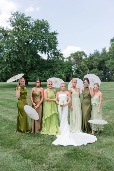 Bridal party portrait with bridesmaids in green dresses surrounding the bride, paper parasols adding a playful accent to the coordinated look.