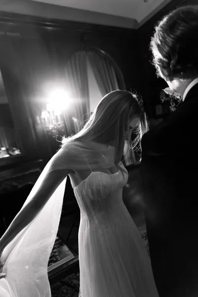 Bridal portrait of a bride with veil, gently holding the soft tulle as she looks down, framed by warm lamp light and wood paneling.