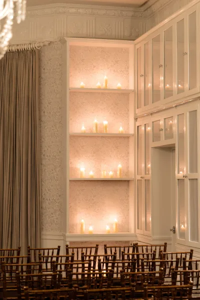 Indoor ceremony decor with a candlelit ceremony backdrop on built-in shelves and glass-front cabinets, flanked by chiavari chairs