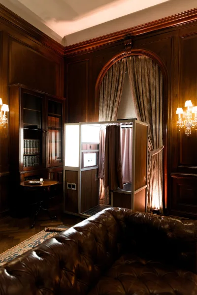 Wedding photo booth featuring an enclosed photo booth with a leather sofa against wood-paneled walls and an arched window