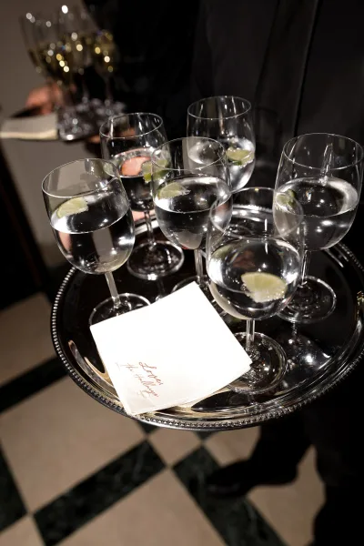 Tray passed drinks at a wedding cocktail hour arranged on a silver tray, set against a checkered tile floor.