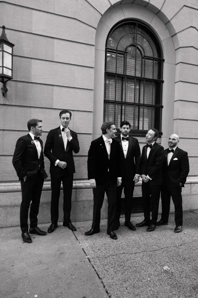 Groomsmen portrait of the groom with groomsmen in classic tuxedos, posed beside an arched window set in a stone wall.