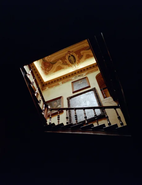 Ornate staircase, a wedding venue staircase crowned by a ceiling fresco, its steps descending through moody stairwell shadows on plaster walls.