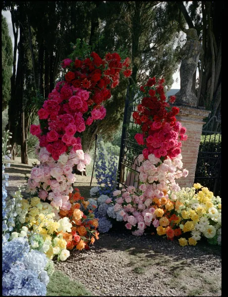 Ceremony floral installation of floral pillars for a wedding, rich with roses by a wrought iron gate amid trees and a brick pillar.